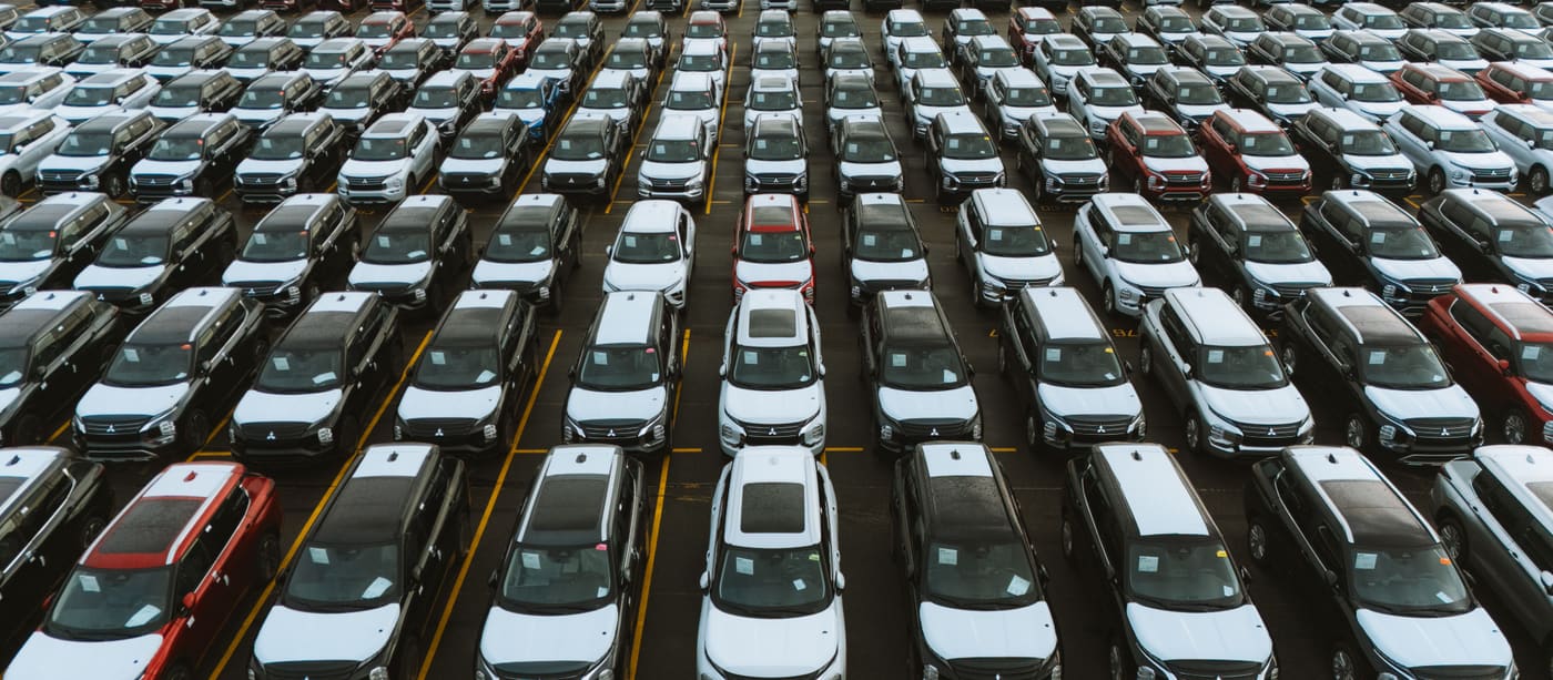 Aerial view of a vehicle storage lot with cars parked in long, even rows.