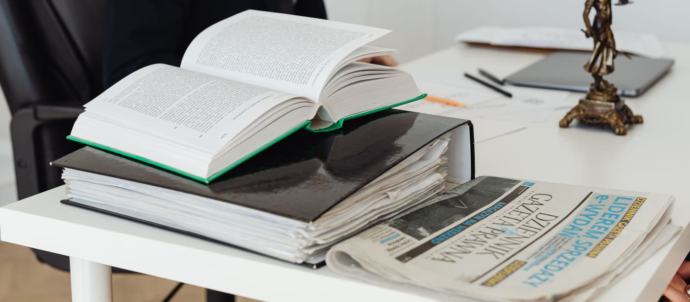 A desk with stacked legal reference books, loose documents and a newspaper.