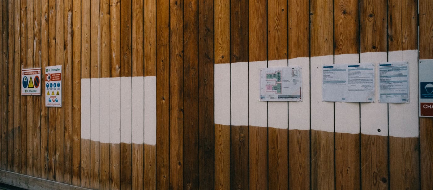 Printed notices and leaflets stapled to a wooden hoarding on a street.