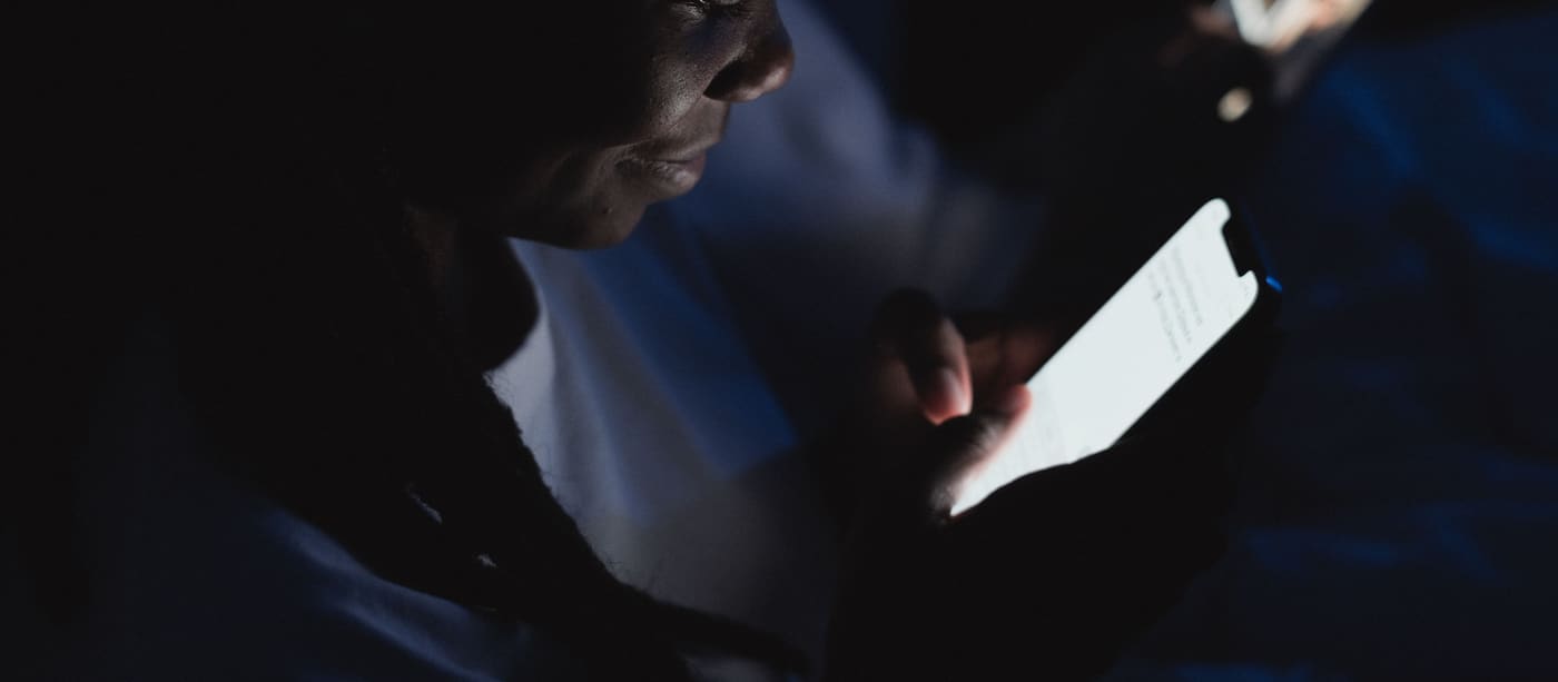 A person reading on a smartphone in a dark room, their face lit only by the screen.