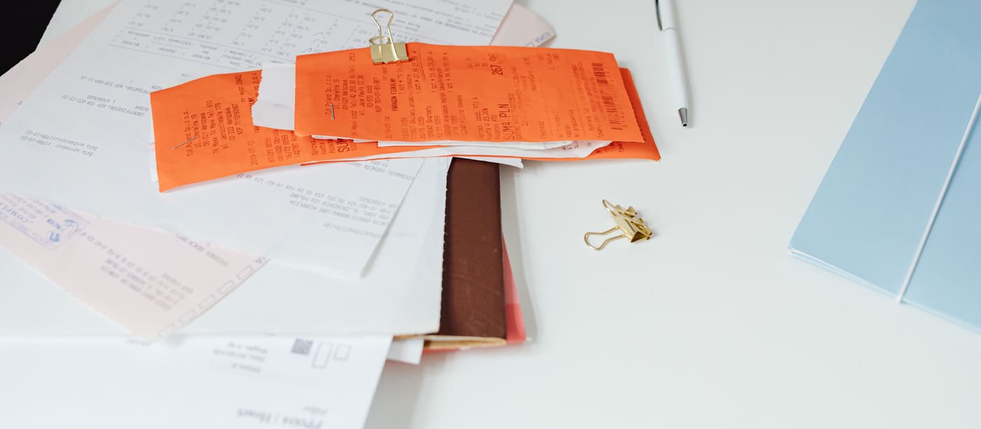 Paper receipts and printed documents arranged on a desk beside office stationery.