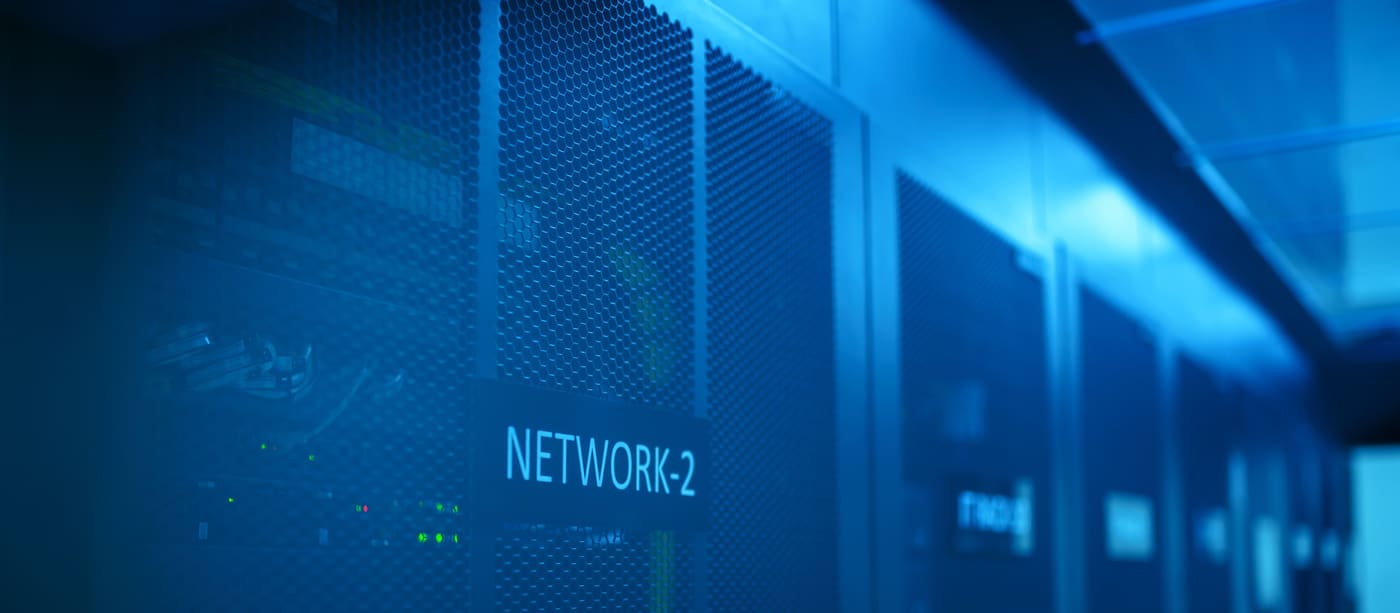 Racks of network equipment in a dimly lit server room, lit blue by their indicators.
