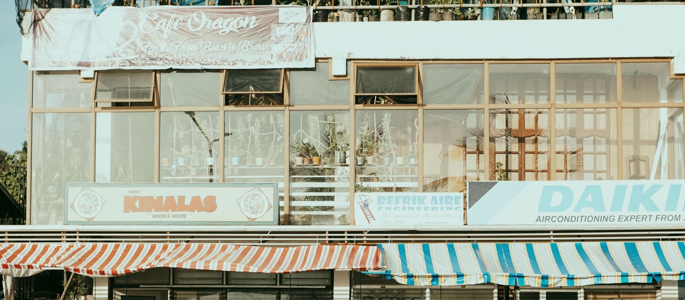 A street of small independent shops with striped awnings and plants on the pavement.