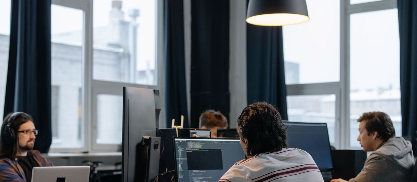 Developers working side by side at desktop computers in an open-plan tech office.