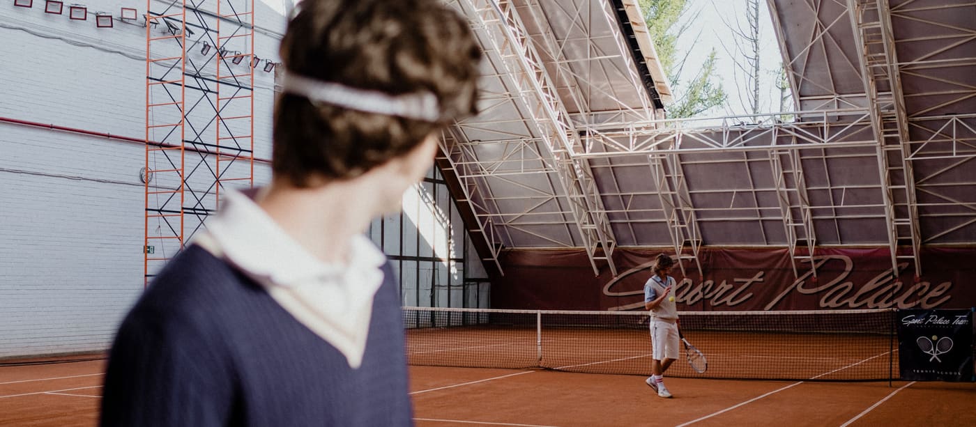 Two players mid-rally on an indoor clay tennis court during a competitive match.