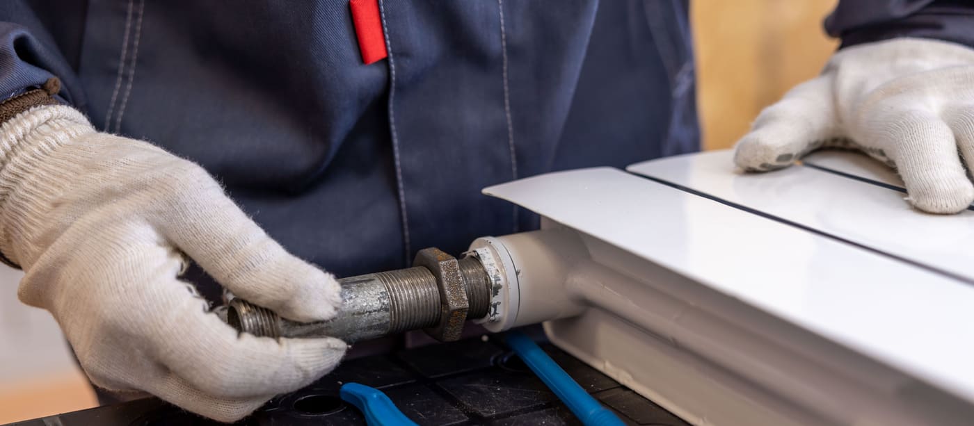 Close-up of a plumber's hands fitting a radiator pipe with a wrench.